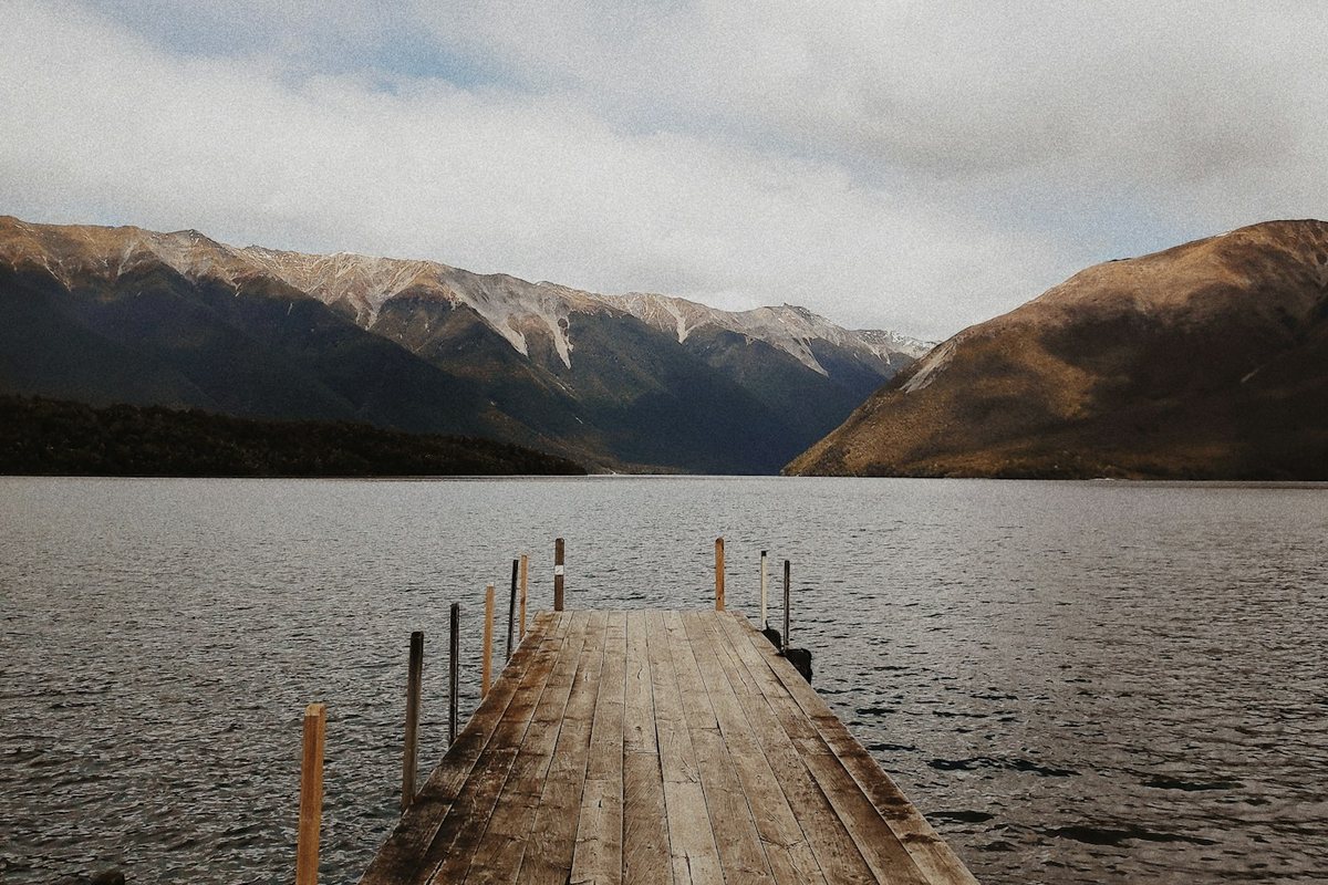 brown wooden dock on lake near mountain under white clouds during daytime