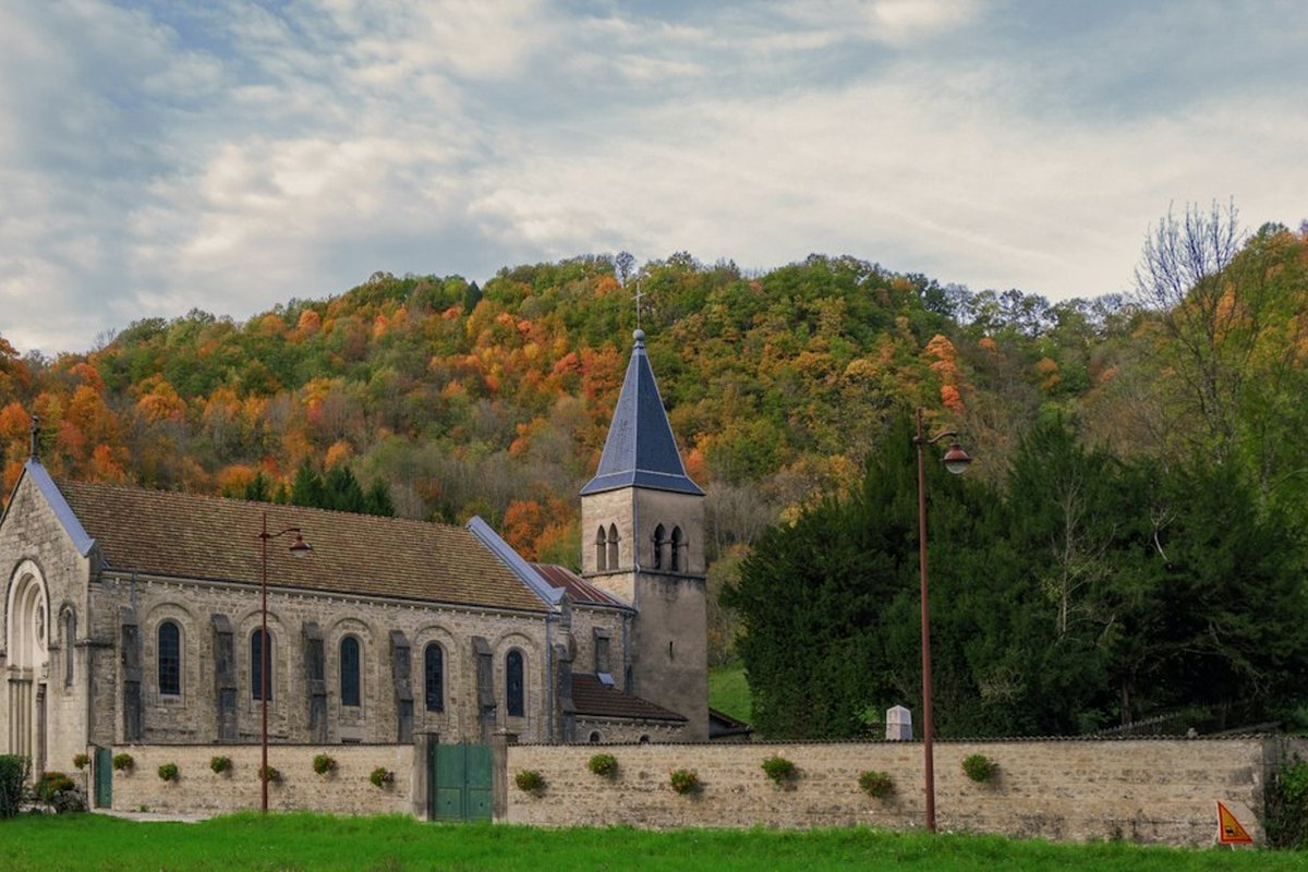 A small stone church in a green field with autumn hills