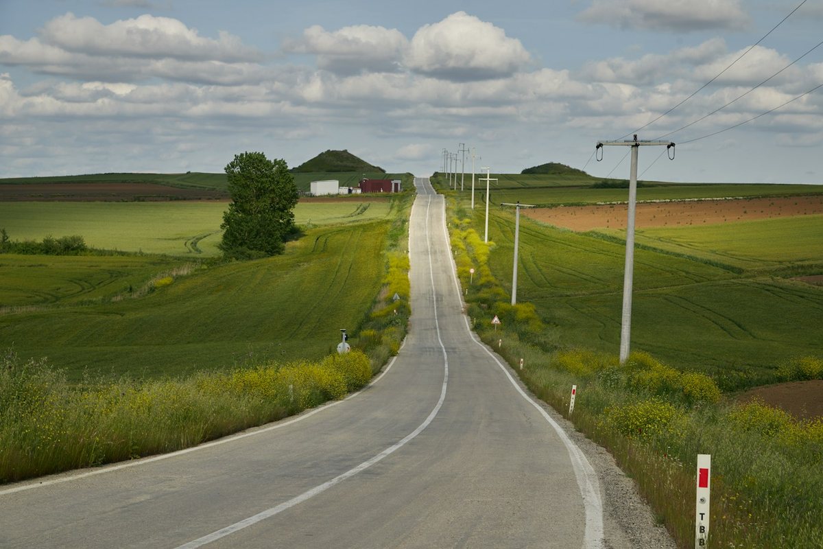 an empty road in the middle of a green field